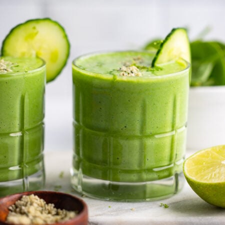 pineapple cucumber smoothie in glass with slice of cucumber.