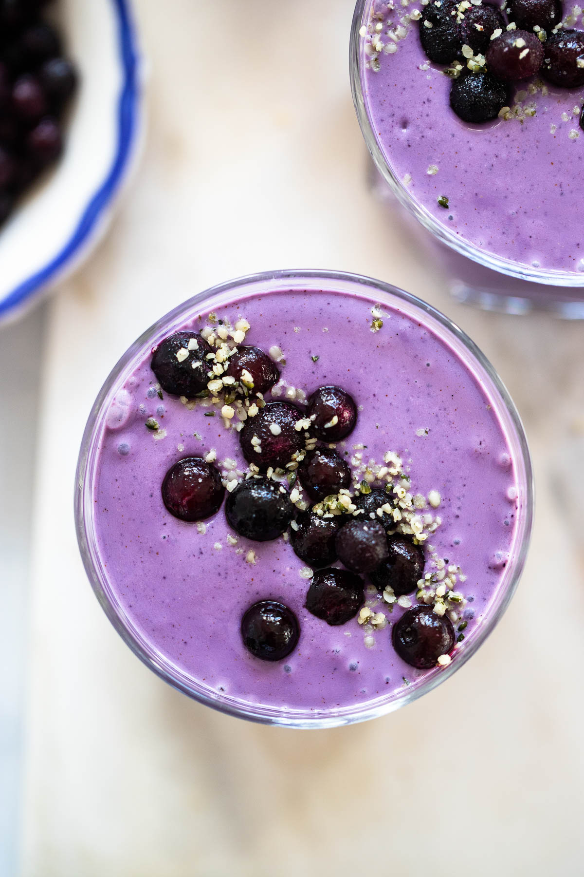 close up photo of the top of blueberry oat smoothie in a glass with frozen blueberries and hemp hearts on top.
