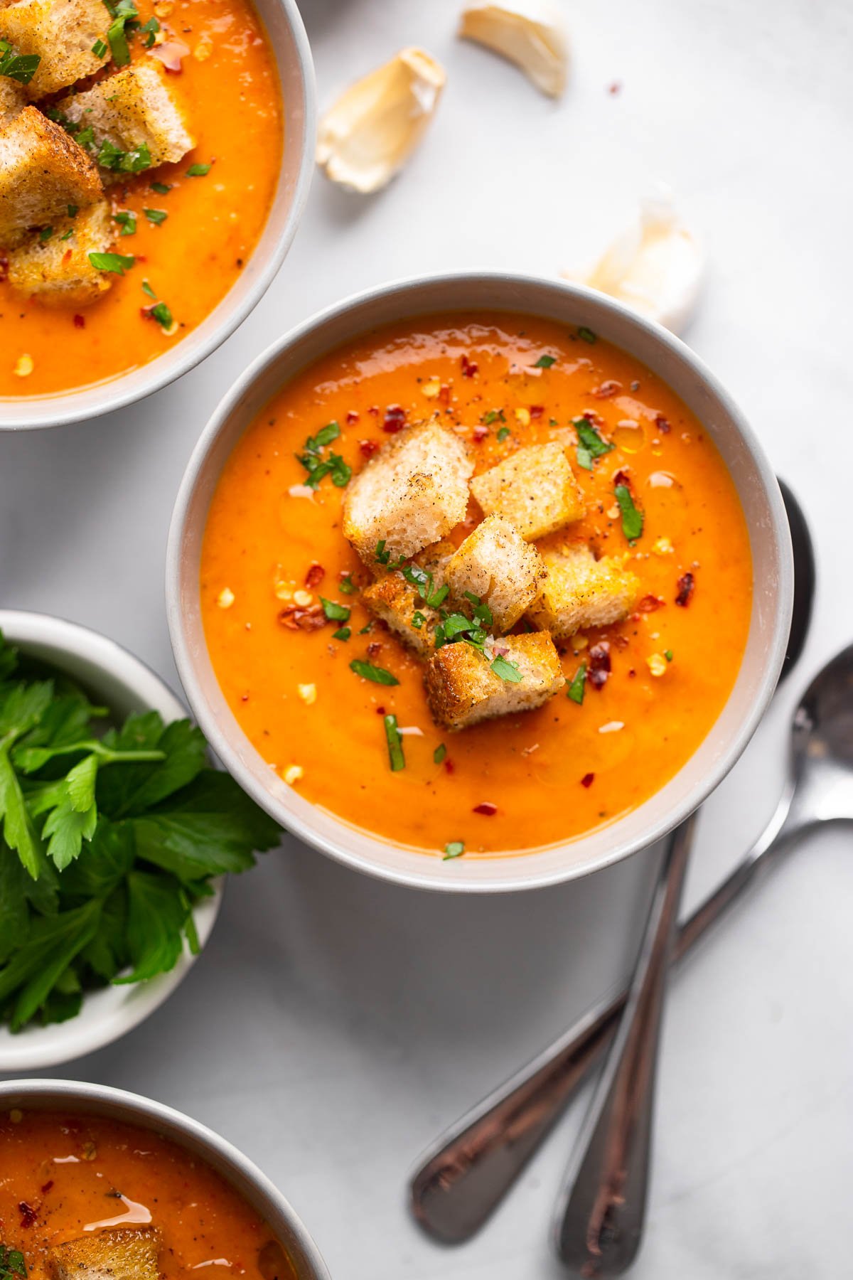 butternut squash and red pepper soup in bowl garnished with croutons and parsley.
