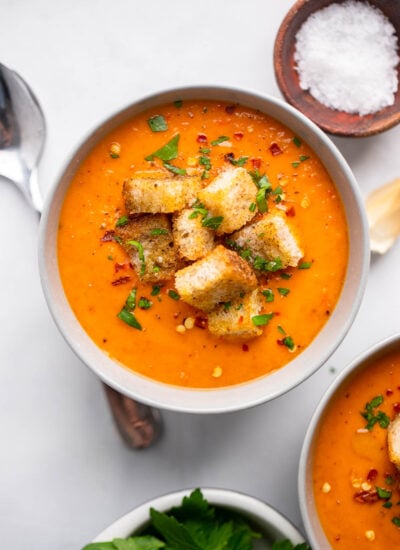 butternut and red pepper soup in bowl garnished with croutons and red pepper flakes.