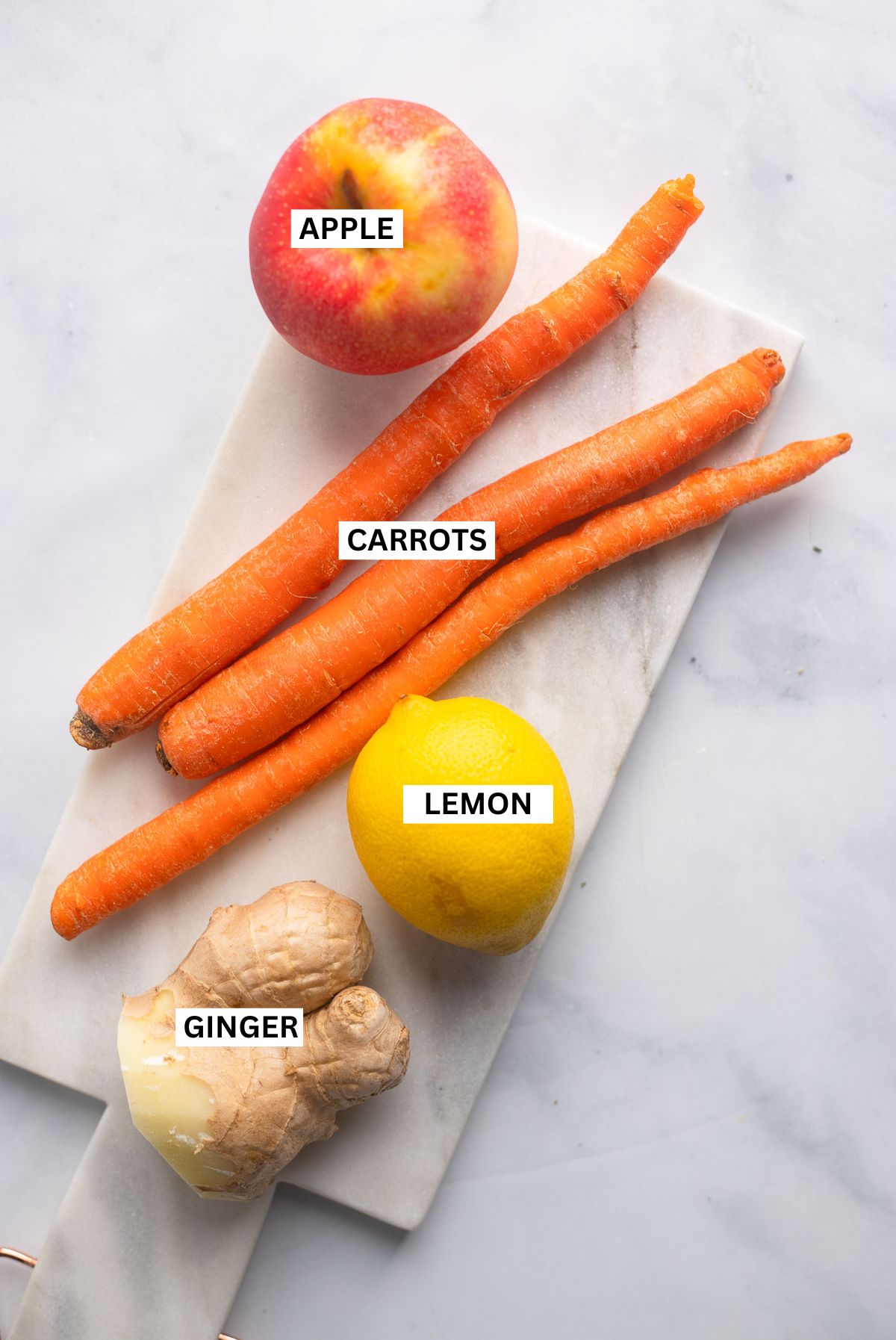 carrot and ginger juice ingredients laid out on white background with labels.