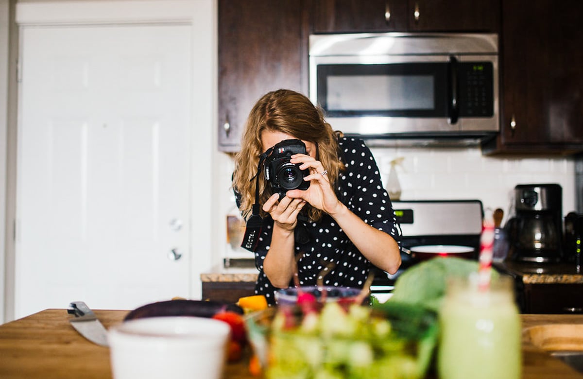 blonde woman standing in kitchen with camera taking pictures. 