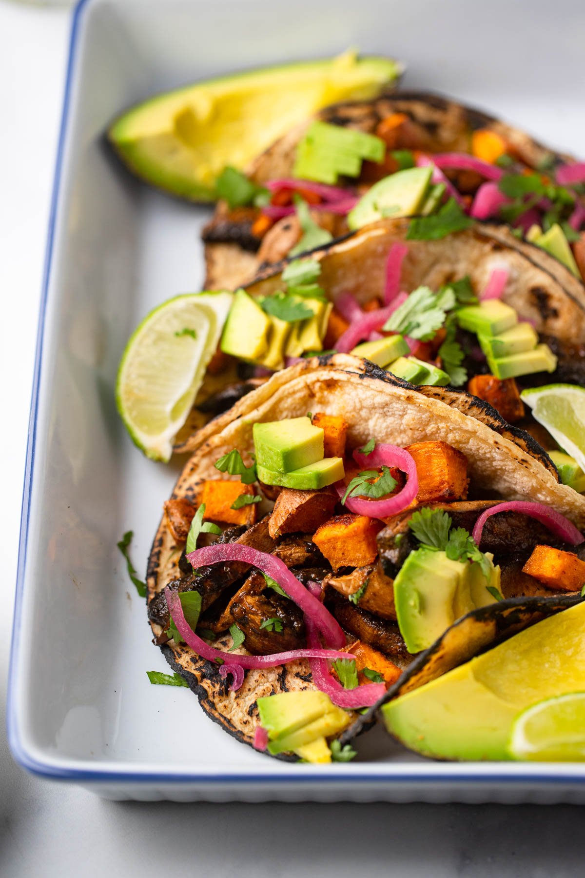 mushroom and sweet potato tacos garnished with sliced avocado, pickled red onion, and chopped cilantro.
