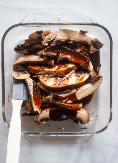 sliced portobello mushrooms in a shallow baking dish with marinade poured over top.