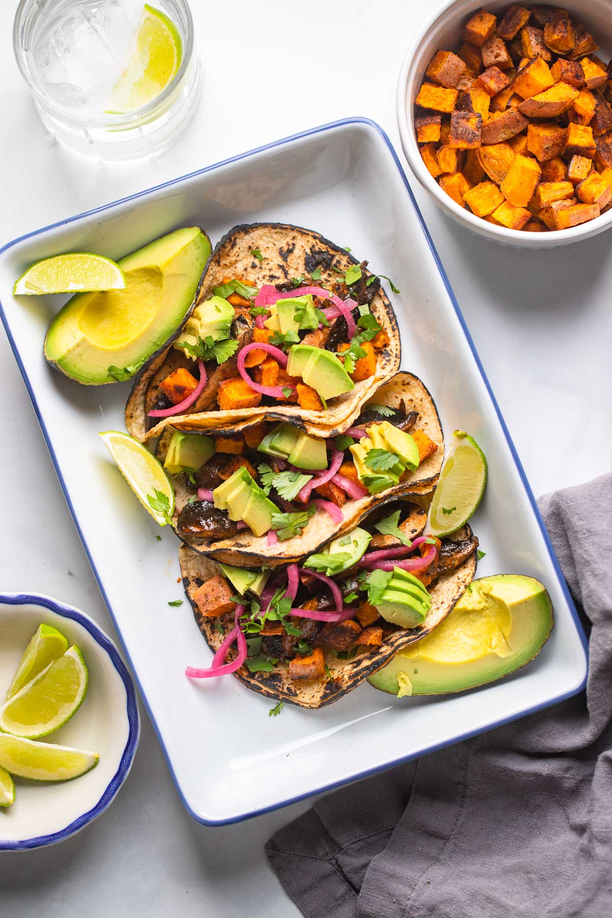 mushroom and sweet potato tacos topped with avocado and cilantro in a shallow tray.