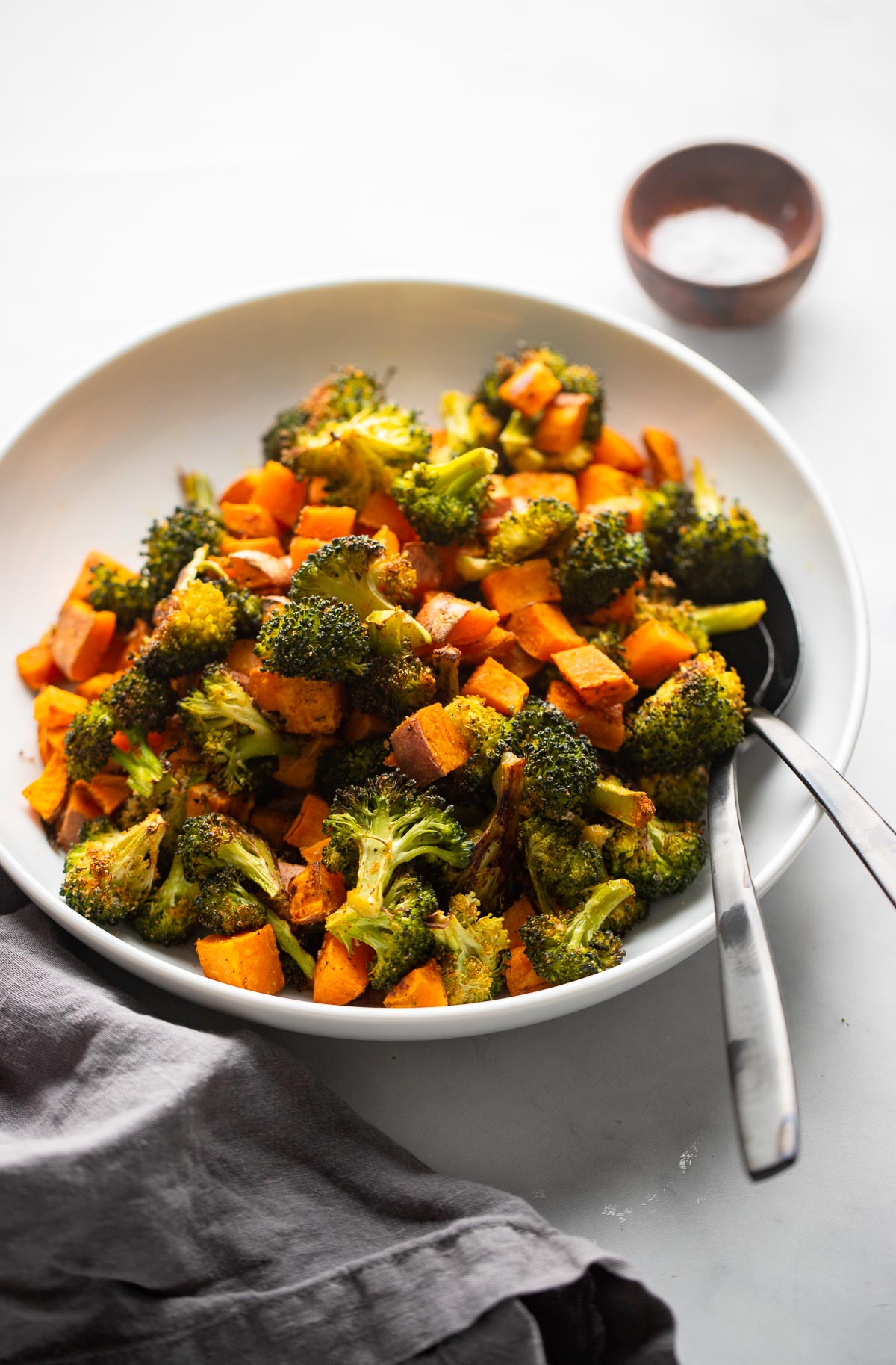 roasted broccoli and sweet potatoes in a large bowl with serving spoons.