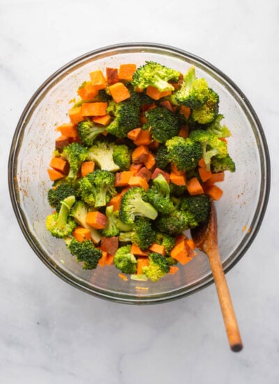 chopped broccoli and sweet potato tossed with olive oil and spices in mixing bowl.