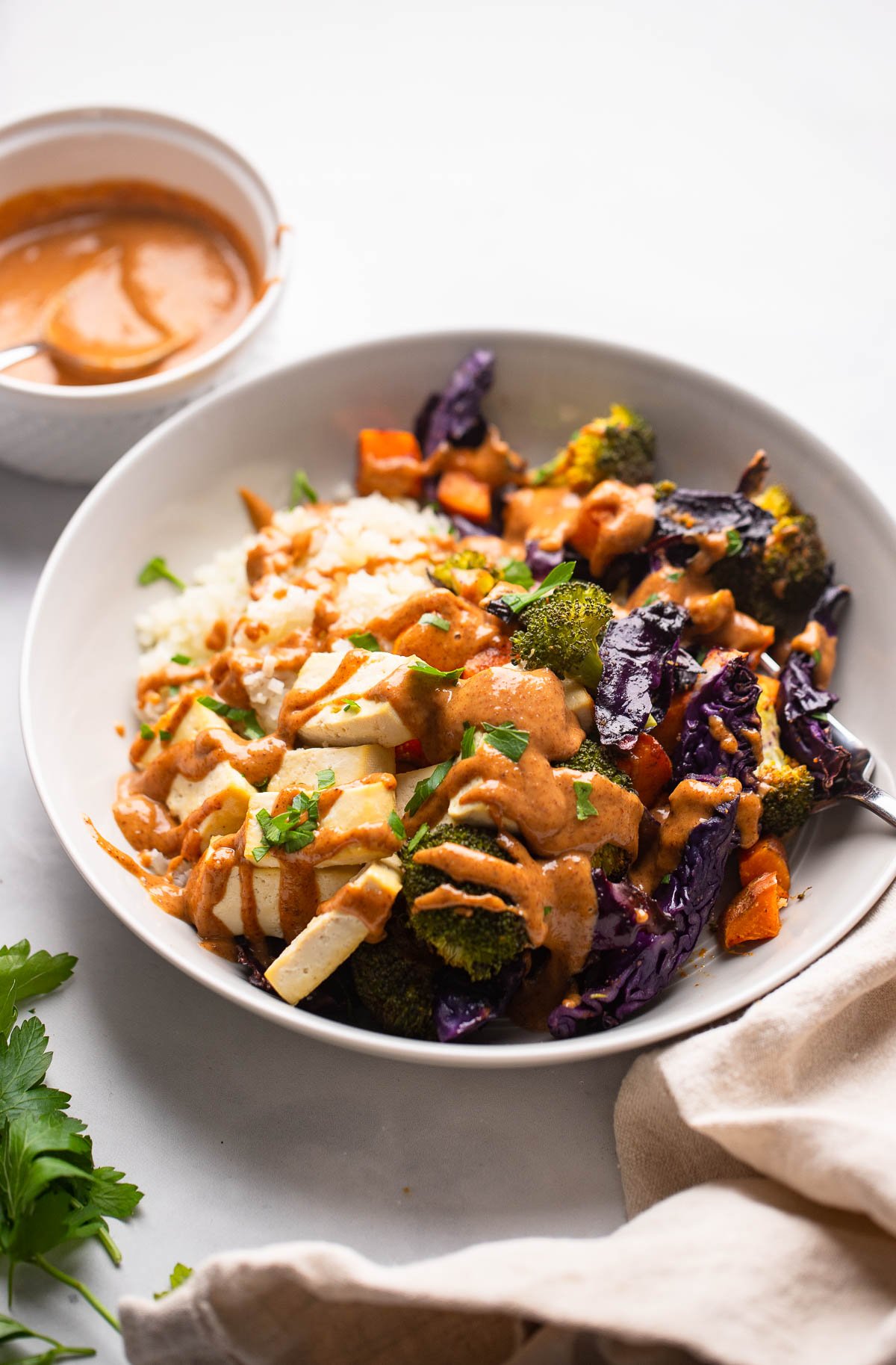 tofu power bowl with roasted vegetables and spicy almond sauce garnished with fresh parsley.