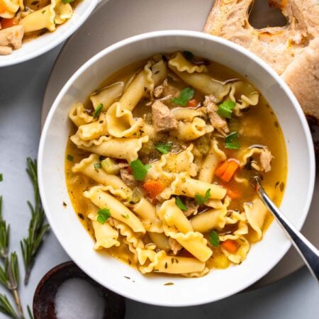 vegan chicken noodle soup in white bowl with fresh parsley as garnish.