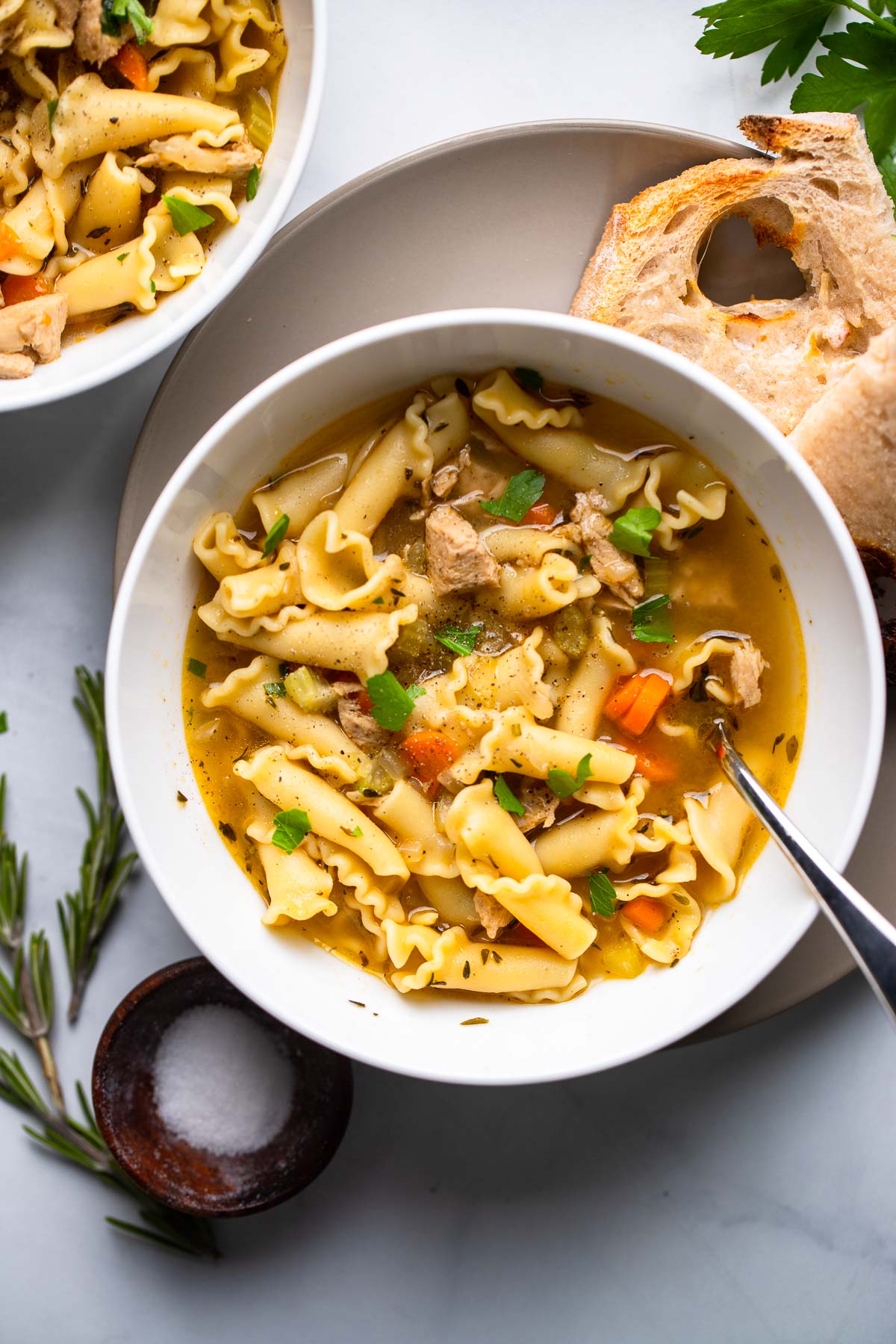 vegan chicken noodle soup in white bowl with fresh parsley as garnish.