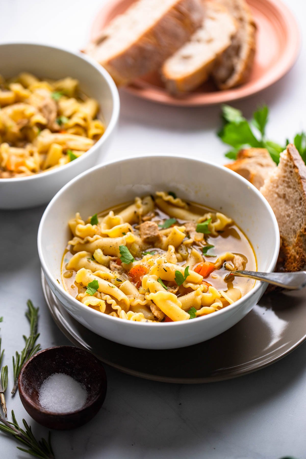 vegan chicken noodle soup in white bowl with bread on the side.