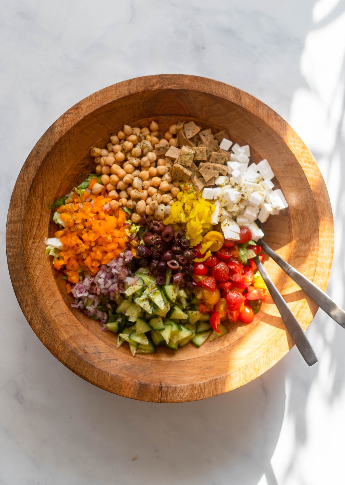 vegan chopped Italian salad in large wooden salad bowl with serving spoons.