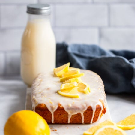 vegan lemon loaf on marble slab with fresh lemon slices.