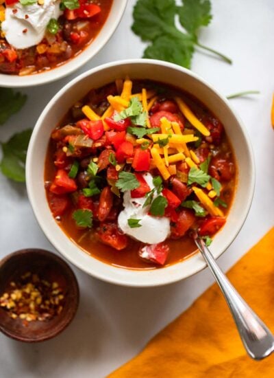 finished chili in bowl garnished with cheese, sour cream, and tomatoes. 