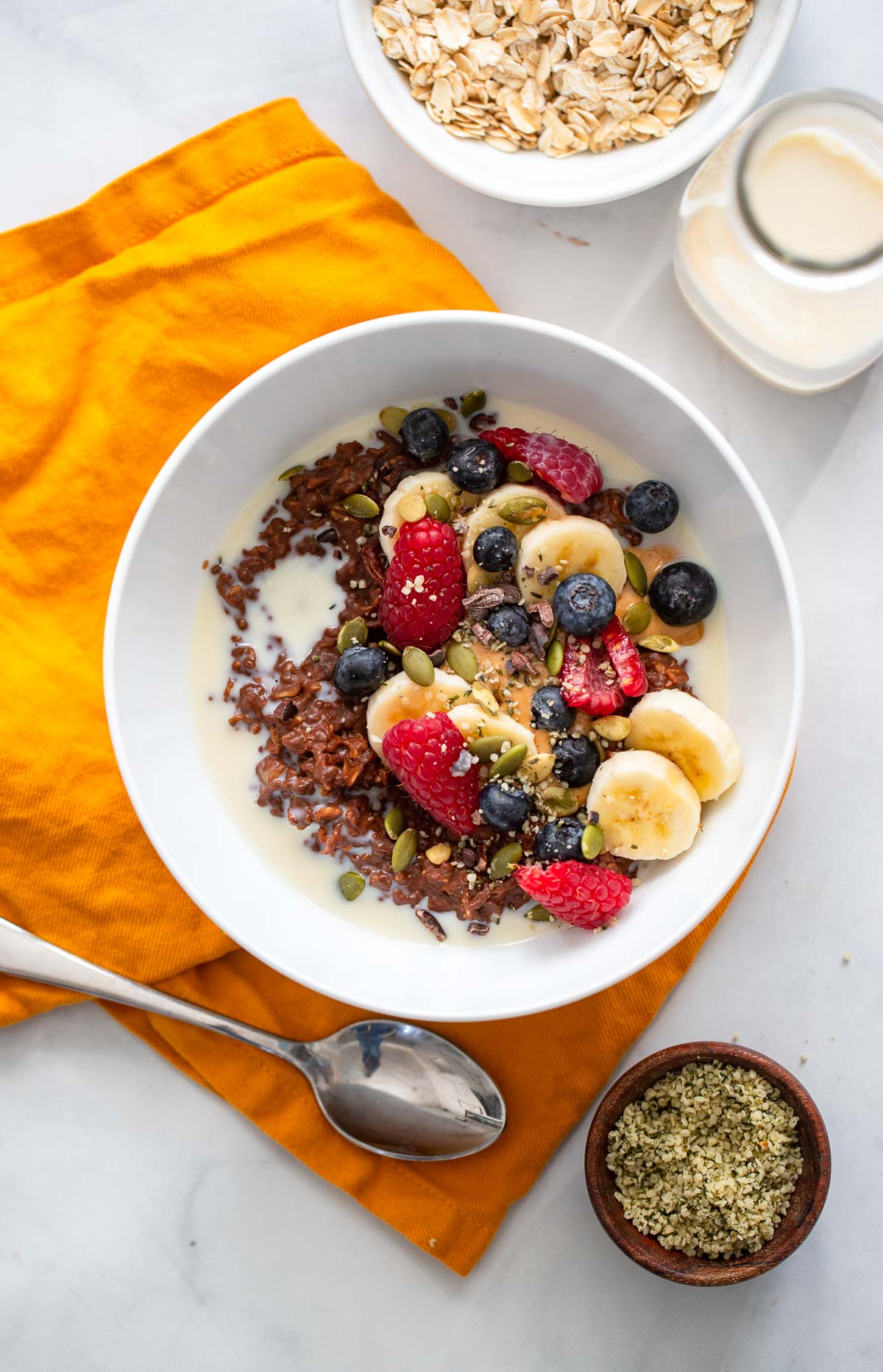 chocolate oatmeal in white bowl topped with fresh berries, peanut butter, and cacao nibs. 