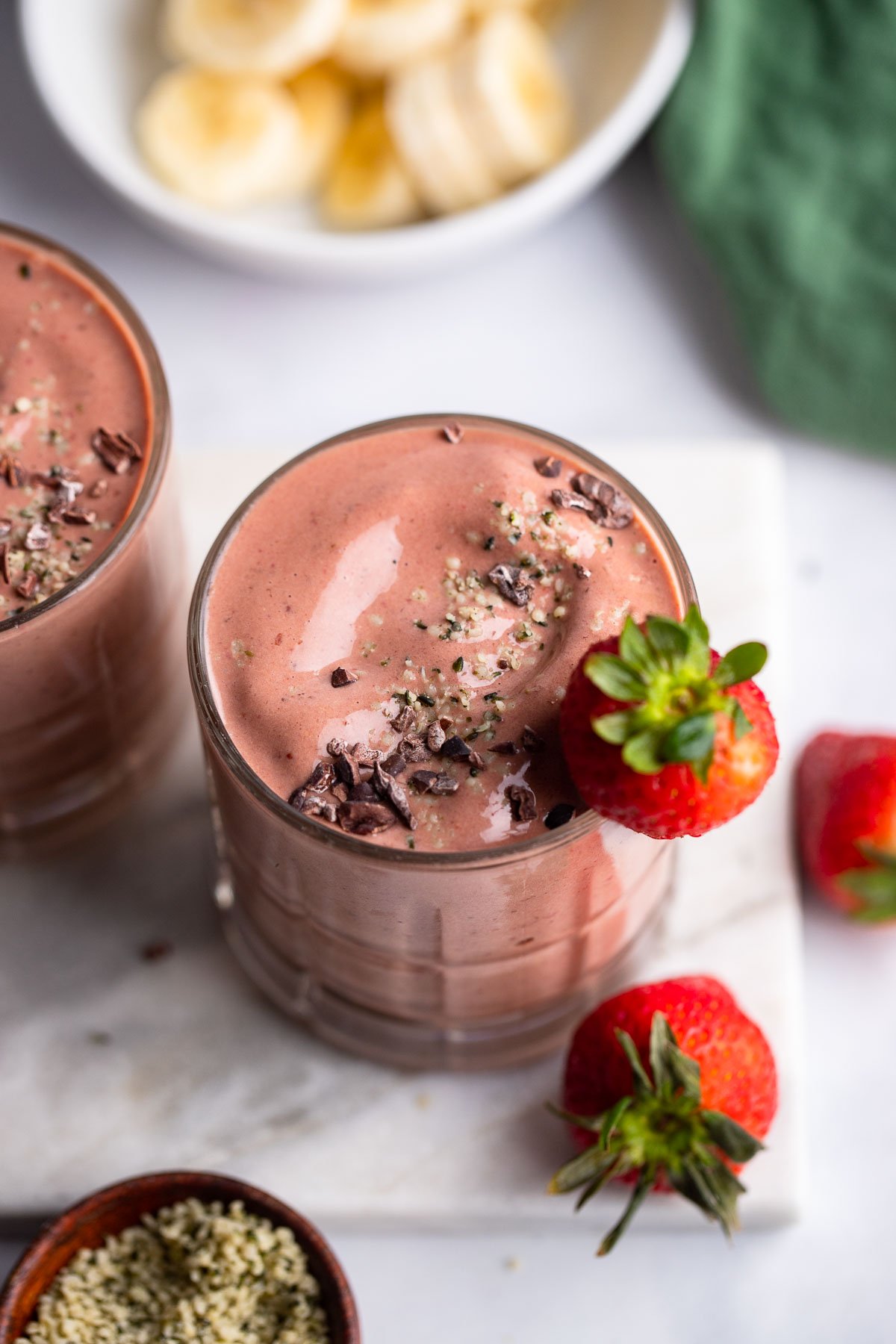 chocolate, strawberry, banana milkshake, garnished with hemp hearts and cocoa beans in a glass.