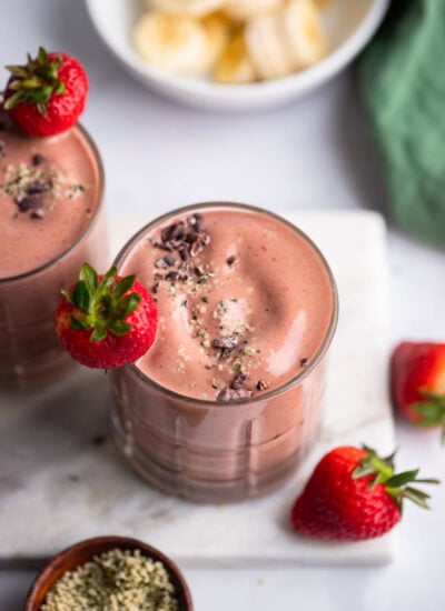 chocolate strawberry banana smoothie divided into two glasses with fresh strawberry as garnish.
