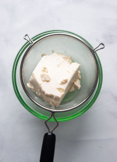 silken tofu in a fine mesh strainer fitted over a mixing bowl. 