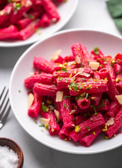 creamy beet pasta in white bowl garnished with parsley and chopped pistachios.