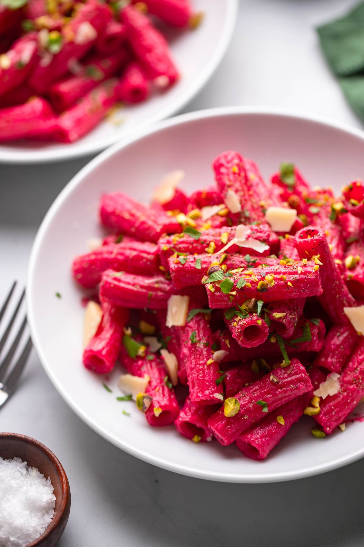 creamy. beet pasta in white bowl garnished with chopped pistachios, parsley, and vegan parmesan.