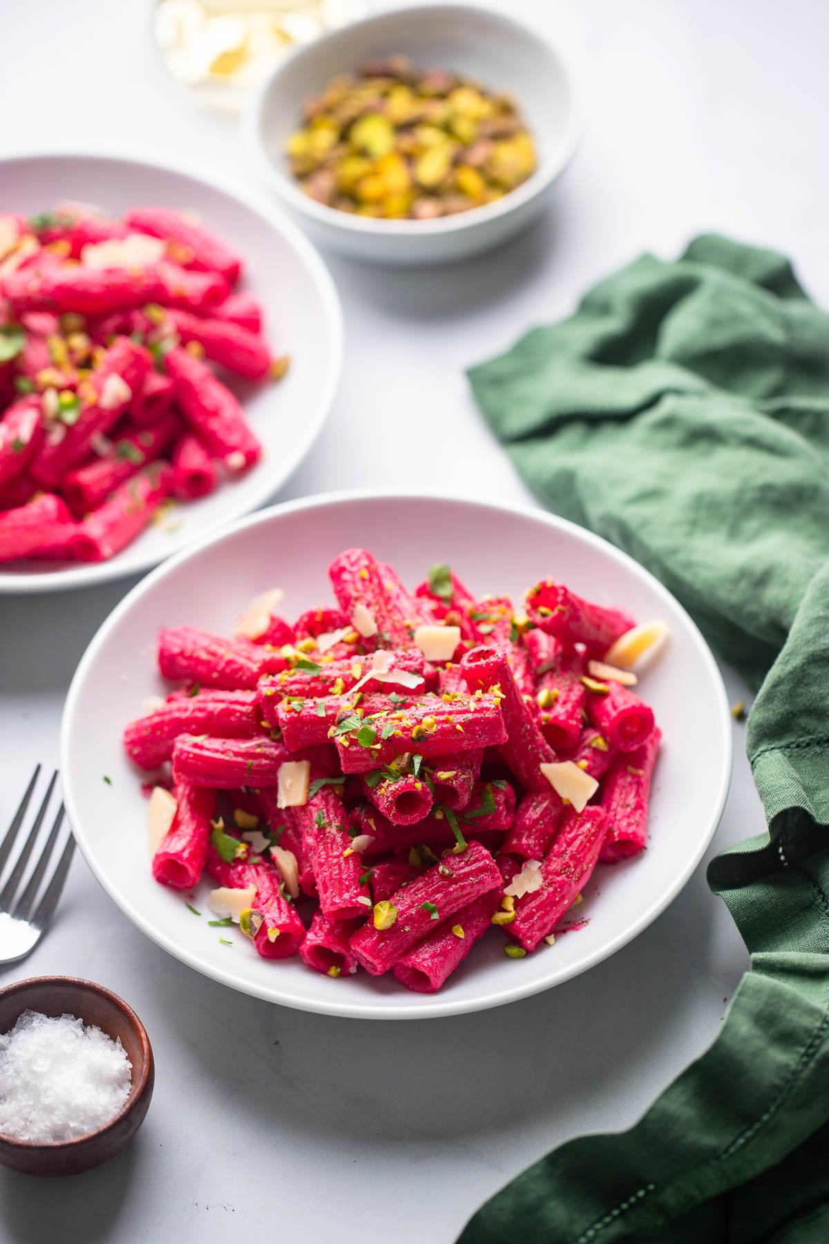 bright pink beet pasta in white bowl with chopped pistachios and parsley for garnish. 
