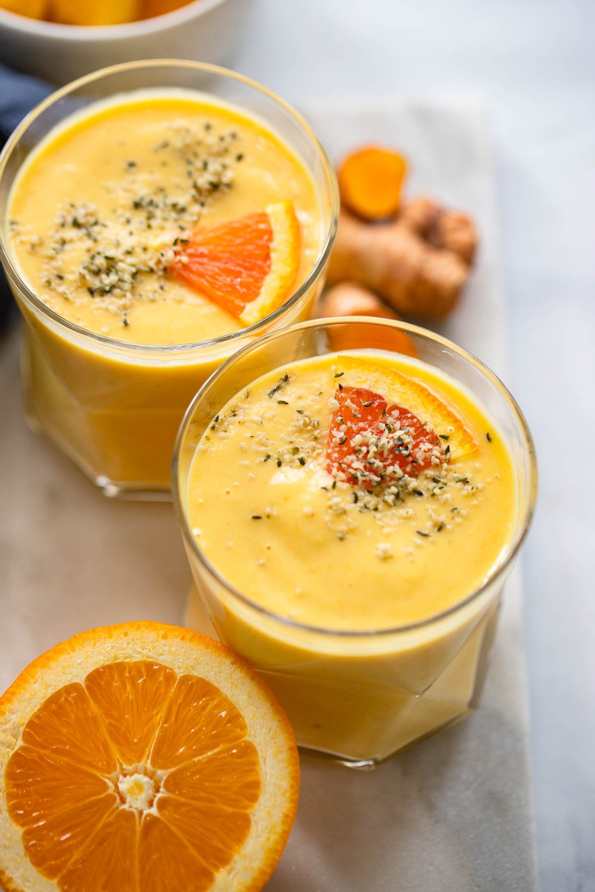 mango turmeric smoothie in glass garnished with hemp hearts and small slice of orange. 