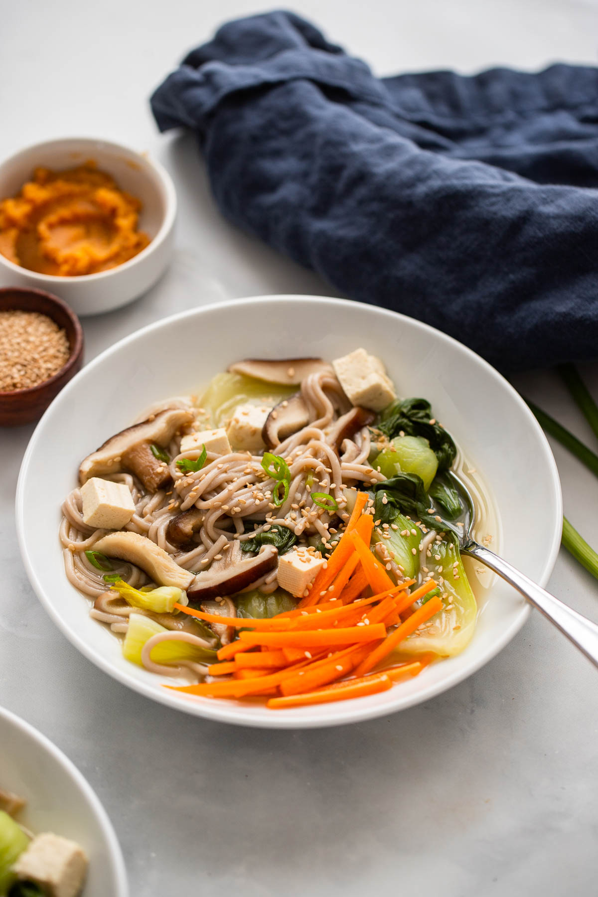 miso soba noodle soup in a bowl garnished with sesame seeds and match stick carrots. 