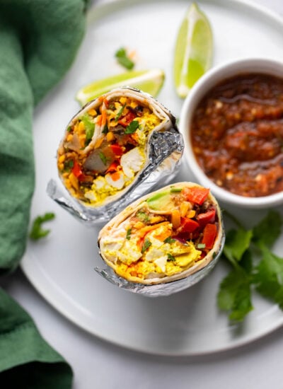 vegan breakfast burrito sliced in half and set up vertically on plate to show the filling.