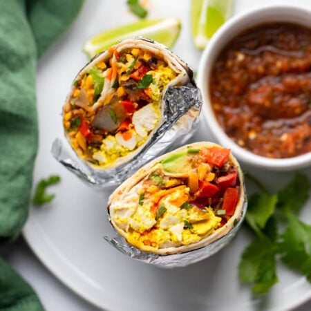 vegan breakfast burrito sliced in half and set up vertically on plate to show the filling.