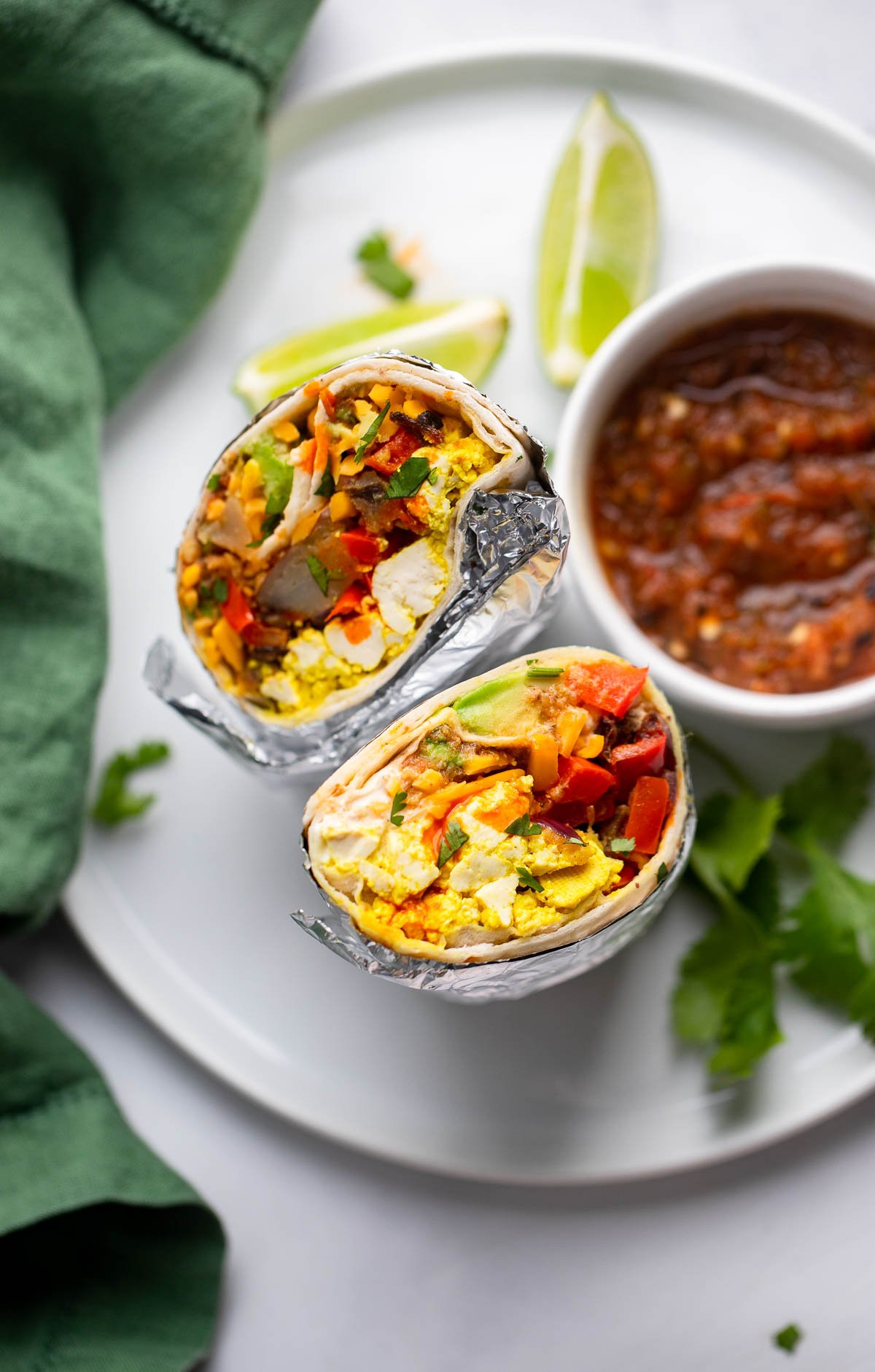 vegan breakfast burrito wrapped in foil and cut in half to show the filling sitting on a plate.