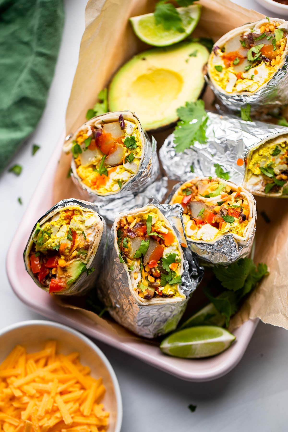 vegan breakfast burritos wrapped in aluminum foil and cut in half to reveal the filling on a tray.
