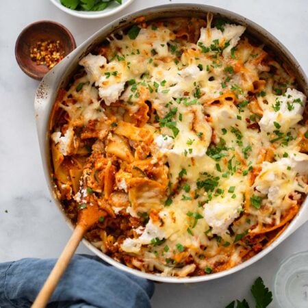 vegan lasagna skillet with wooden spoon and garnished with parsley.