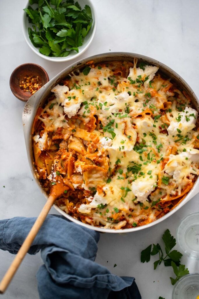 vegan lasagna skillet with wooden spoon and garnished with parsley.