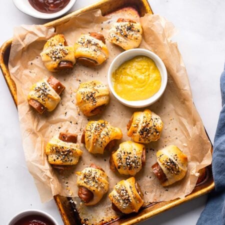 vegan pigs in a blanket on a baking tray with dish of mustard.