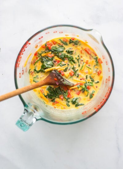 bowl filled with liquid egg, sautéed veggies, and vegan cheese with a wooden spoon.