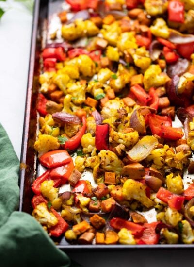 cooked curry roasted vegetables on a sheet pan with green napkin. 