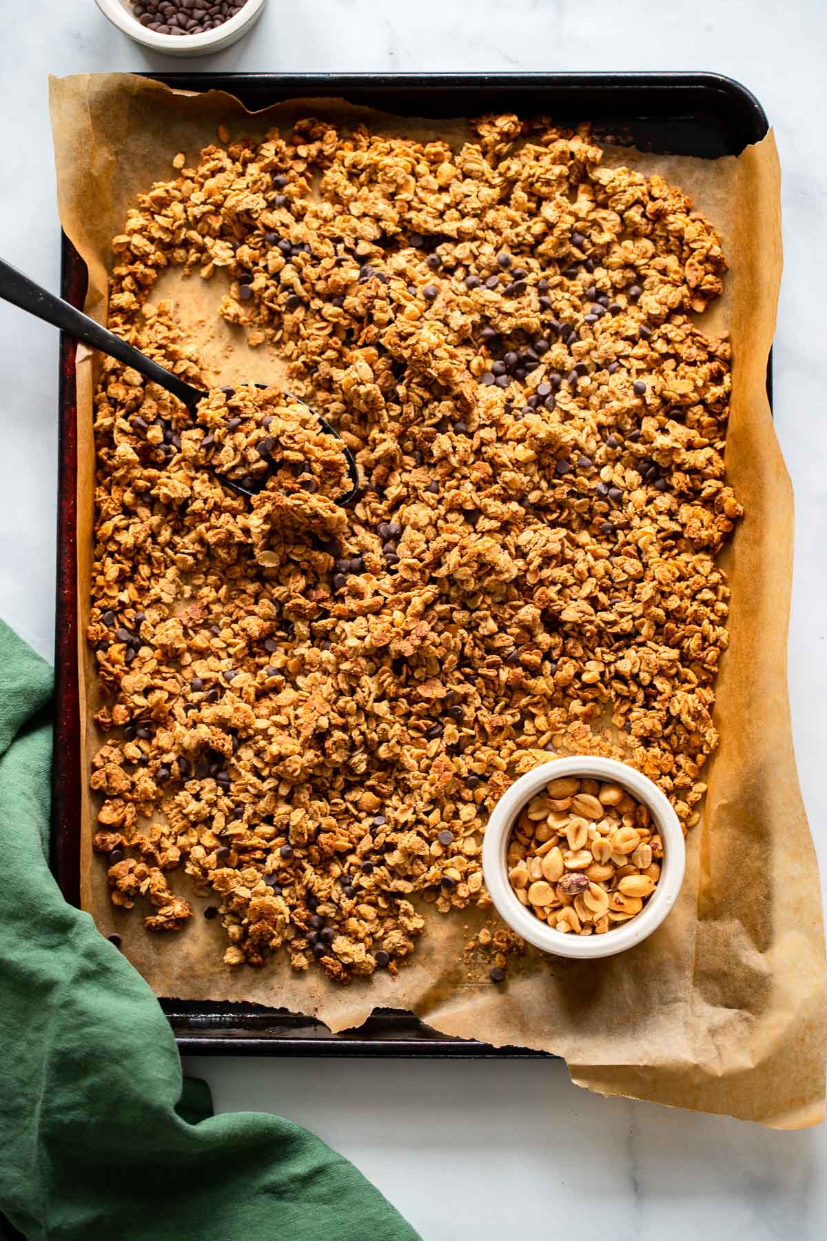Baked Peanut Butter Granola with Mini Chocolate Chips on a parchment paper lined baking sheet. 