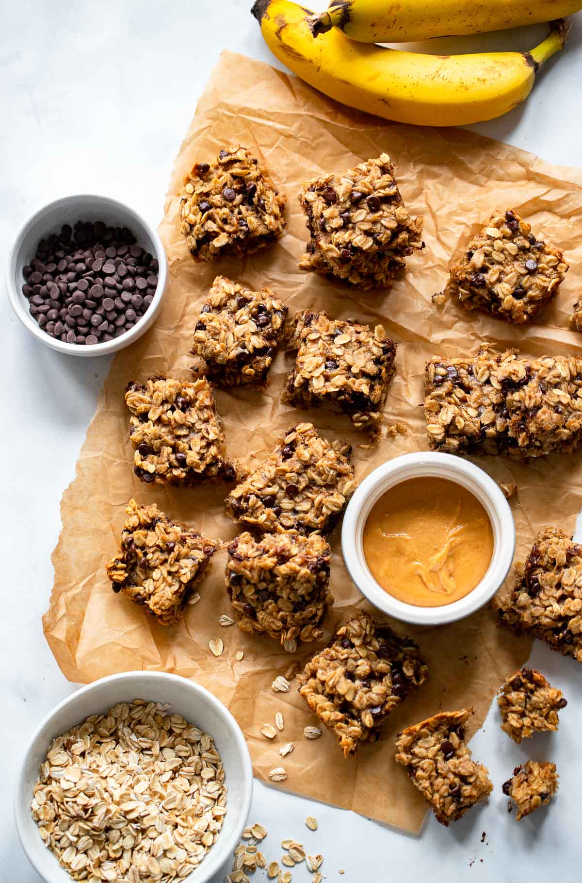 peanut butter banana bars on piece of parchment paper with small dish of peanut butter. 