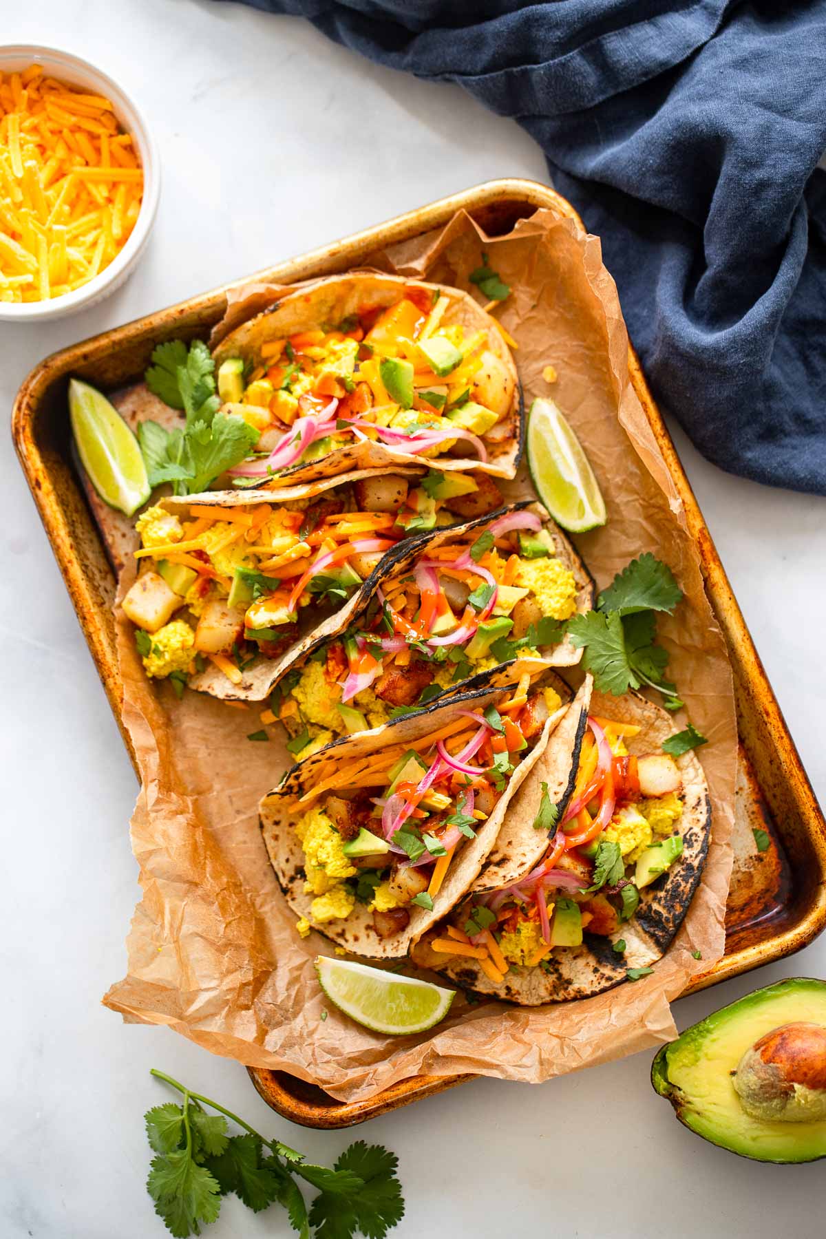 vegan breakfast tacos garnished with cilantro, pickled onions, and avocado in a tray.