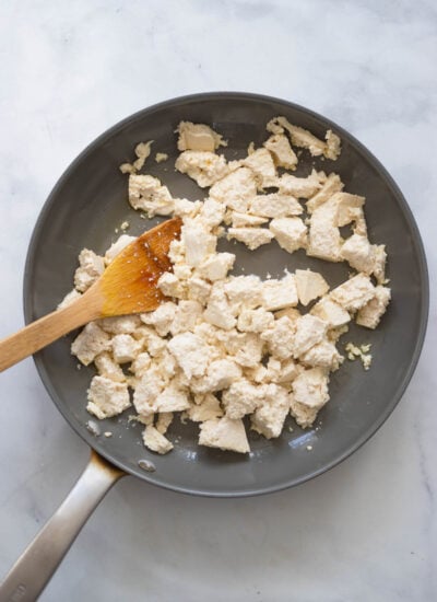 medium firm tofu broken into bite sized pieces in a skillet with a wooden spoon.