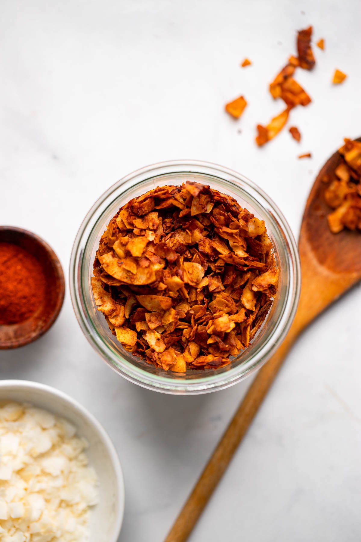 coconut bacon in a jar with a wooden spoon laying next to it.