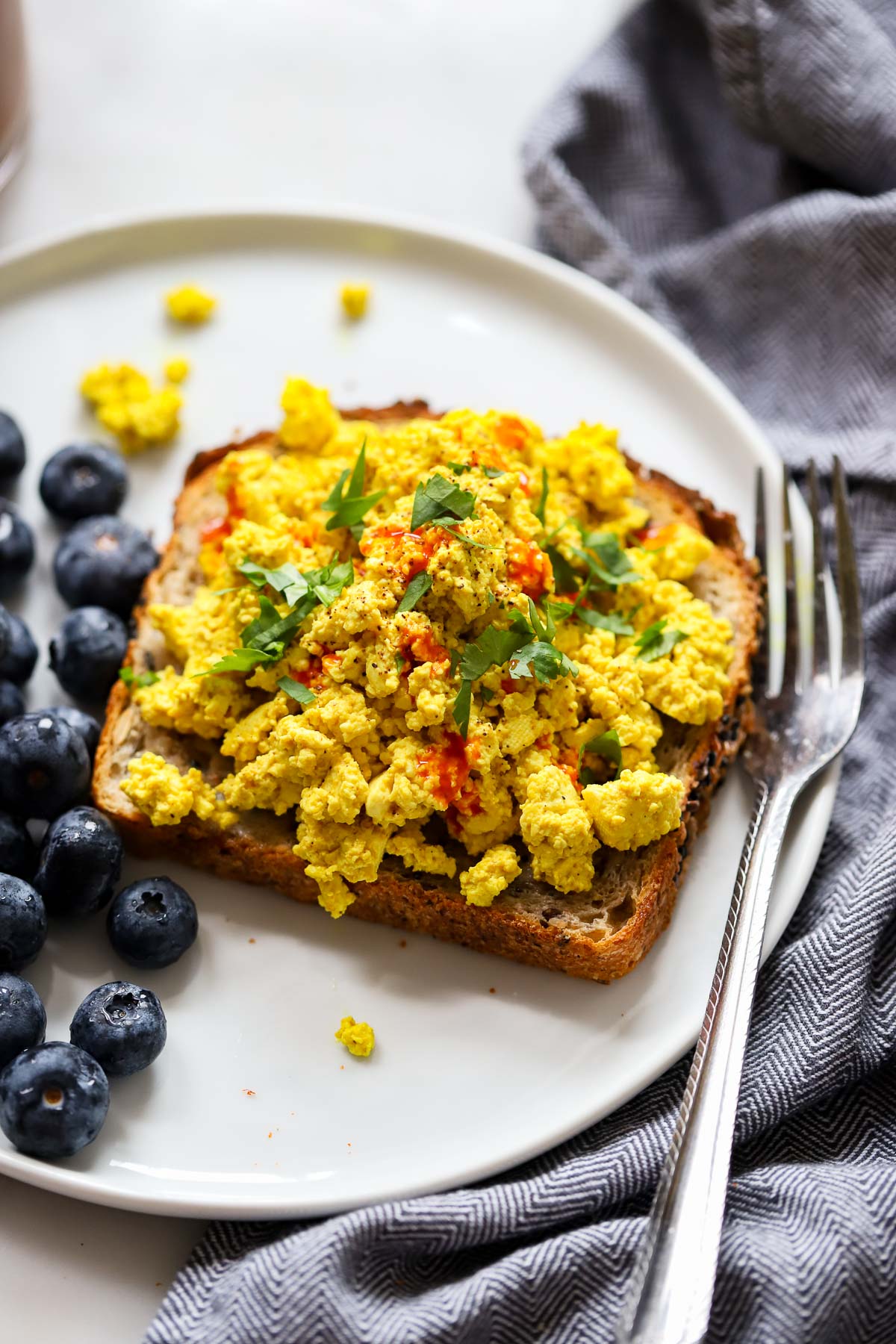 tofu scramble garnished with parsley piled on top of a piece of toast with fresh blueberries on the side. 