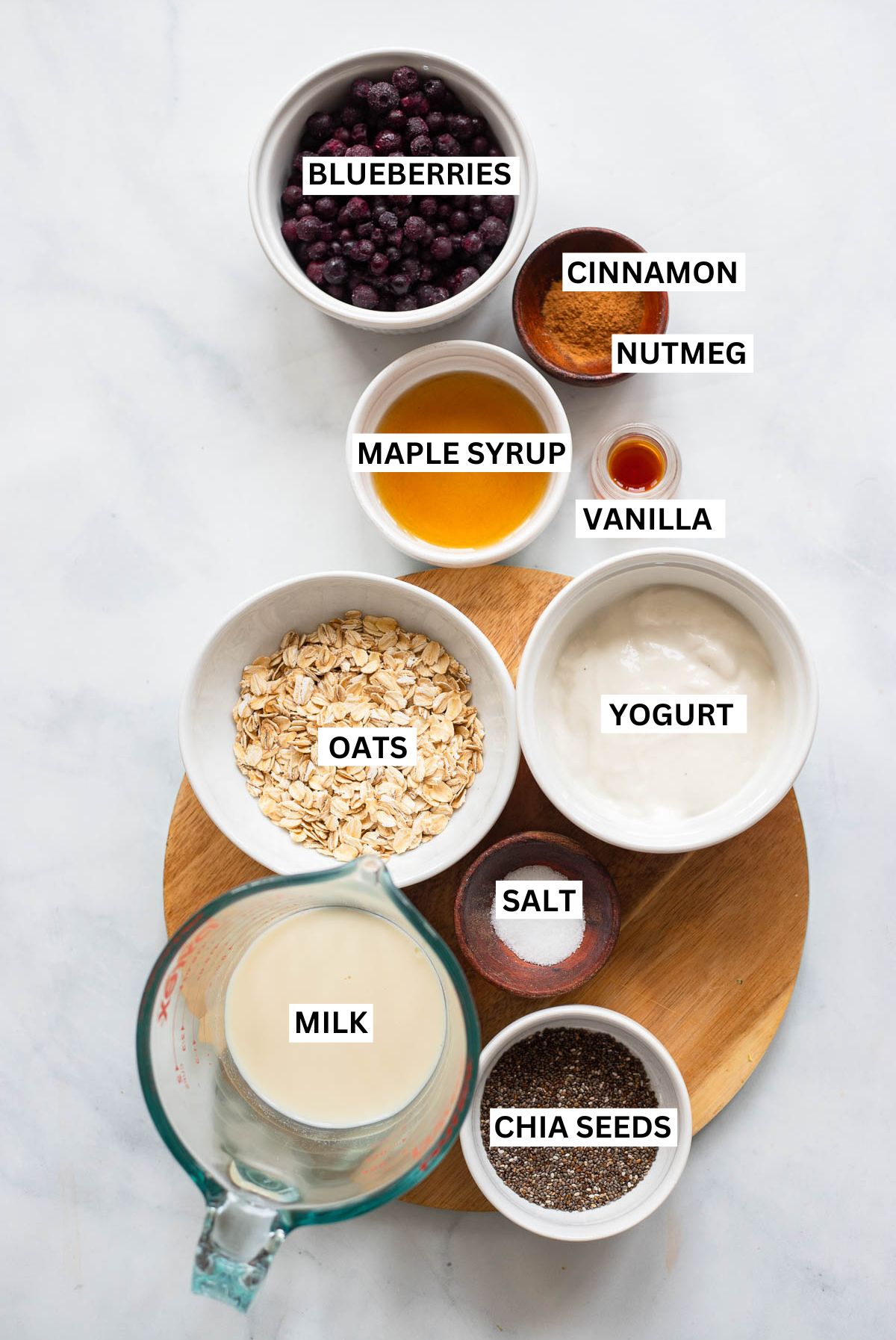 blueberry overnight oats ingredients in small bowls on a white background with text overlay labels. 