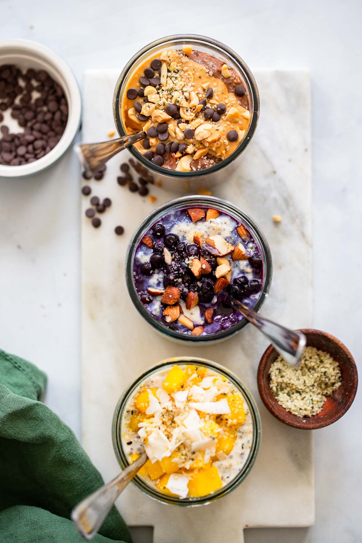 three glasses with different flavors of overnight oats with spoon. 