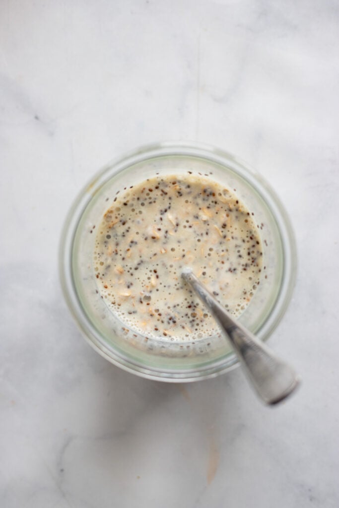 overnight oats ingredients stirred together with a spoon in a glass.