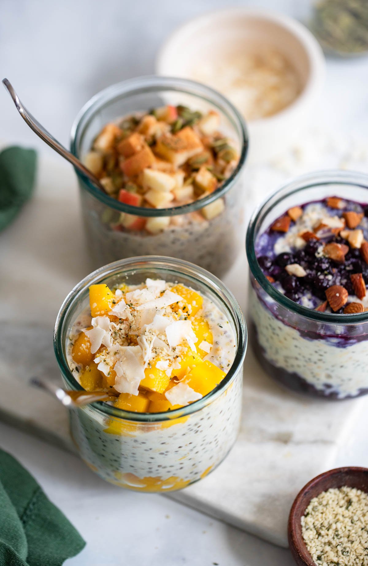 3 glasses of overnight oats with different flavors; mango overnight oats glass is in the foreground. 