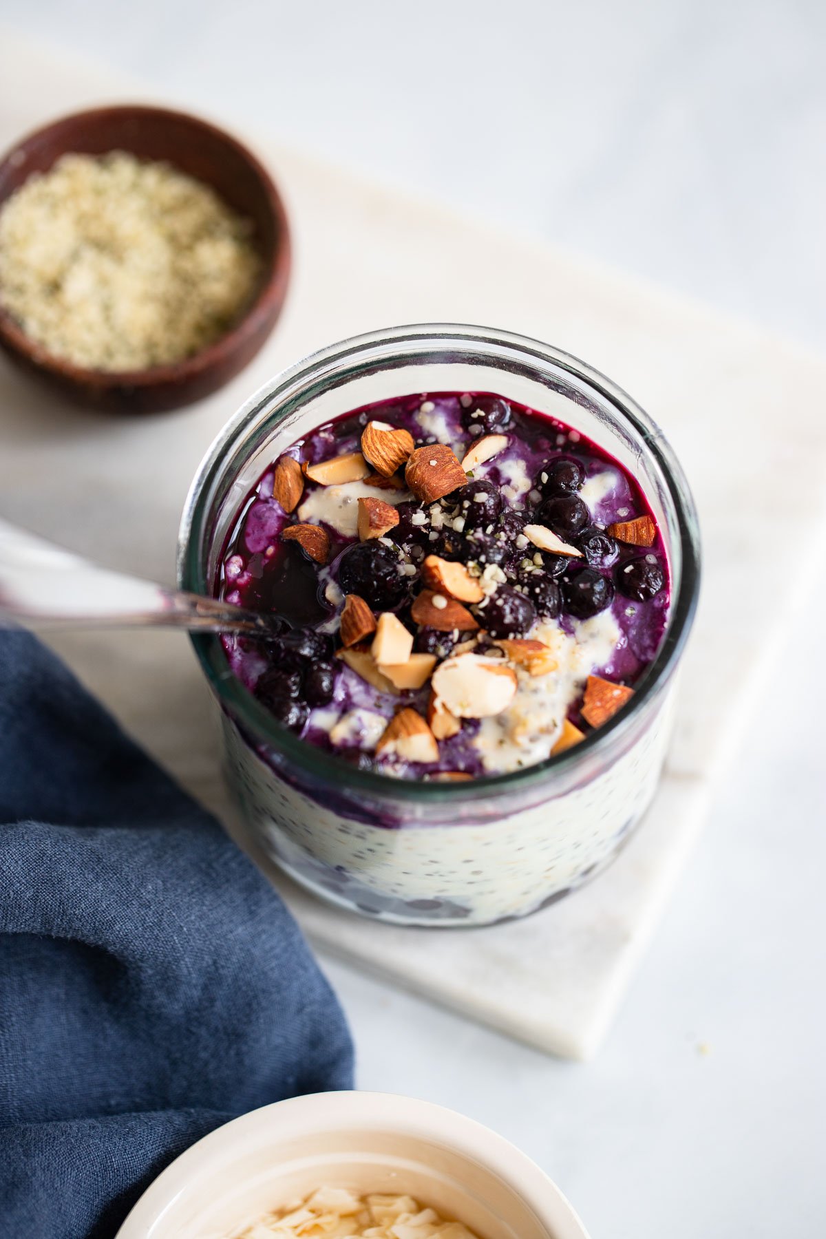blueberry overnight oats topped with chopped almonds and hemp hearts in a glass. 