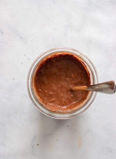 Chocolate overnight oats ingredients mixed in a jar with a spoon.