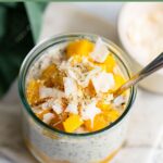 vegan mango overnight oats in a glass jar with a spoon.