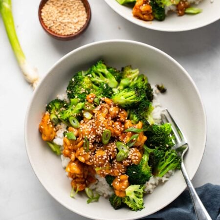 two bowls with rice, broccoli, and sticky tempeh garnished with green onion and sesame seeds.